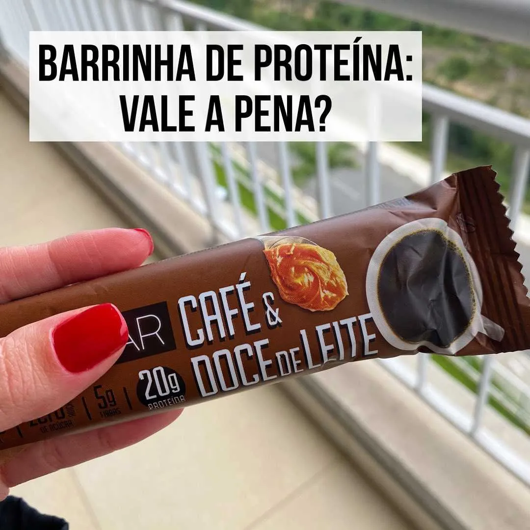 Mão segurando barrinha de proteína sabor café e doce de leite com 20g de proteína na embalagem