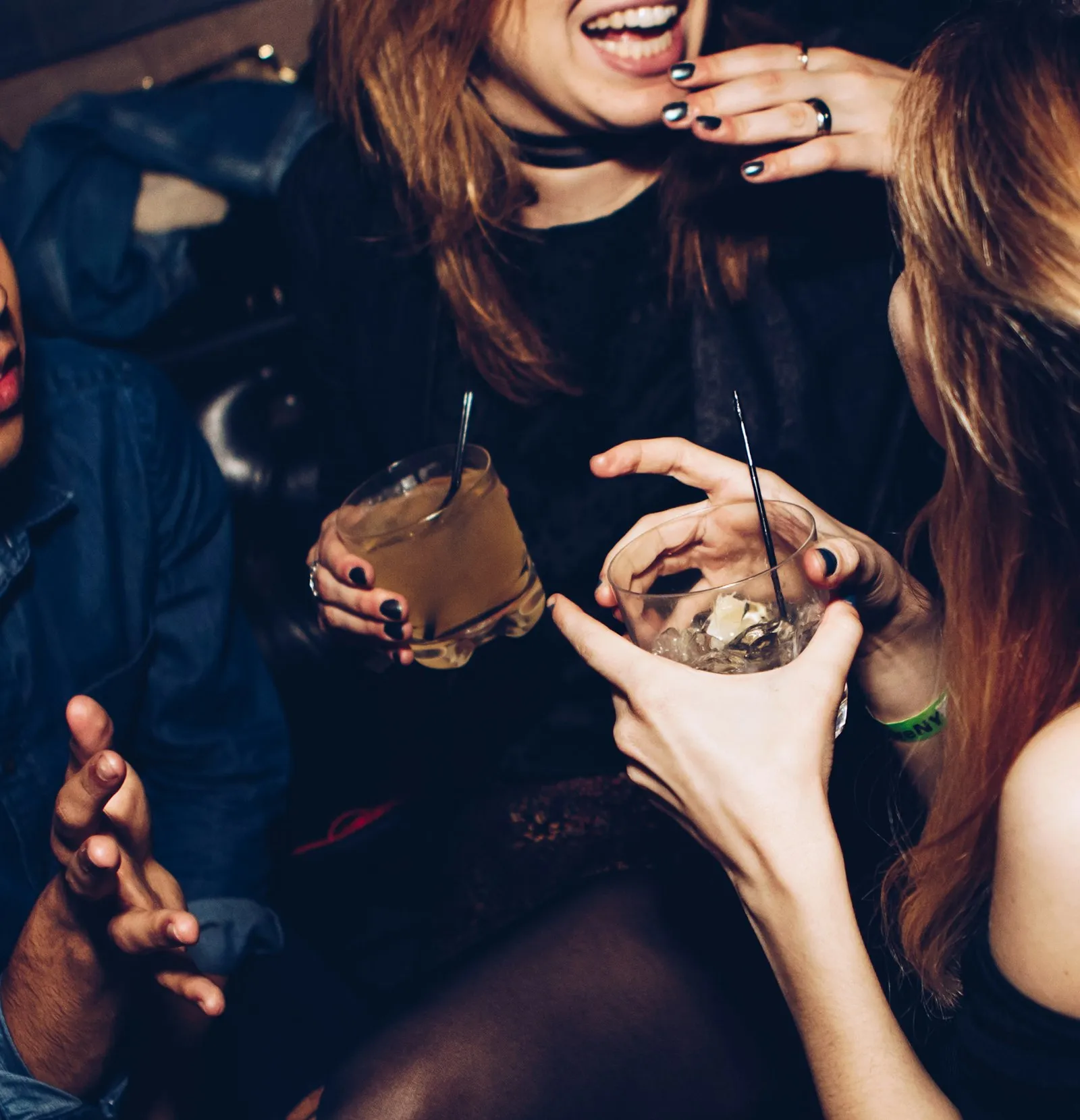 Amigas sorrindo em festa segurando drinks com gelo e canudo, brindando com bebida na balada