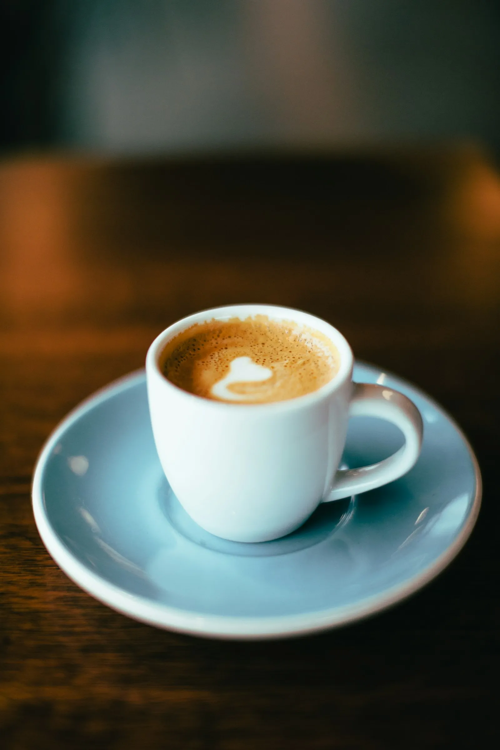 Xícara de café espresso, fonte de cafeína, em pires azul sobre mesa de madeira