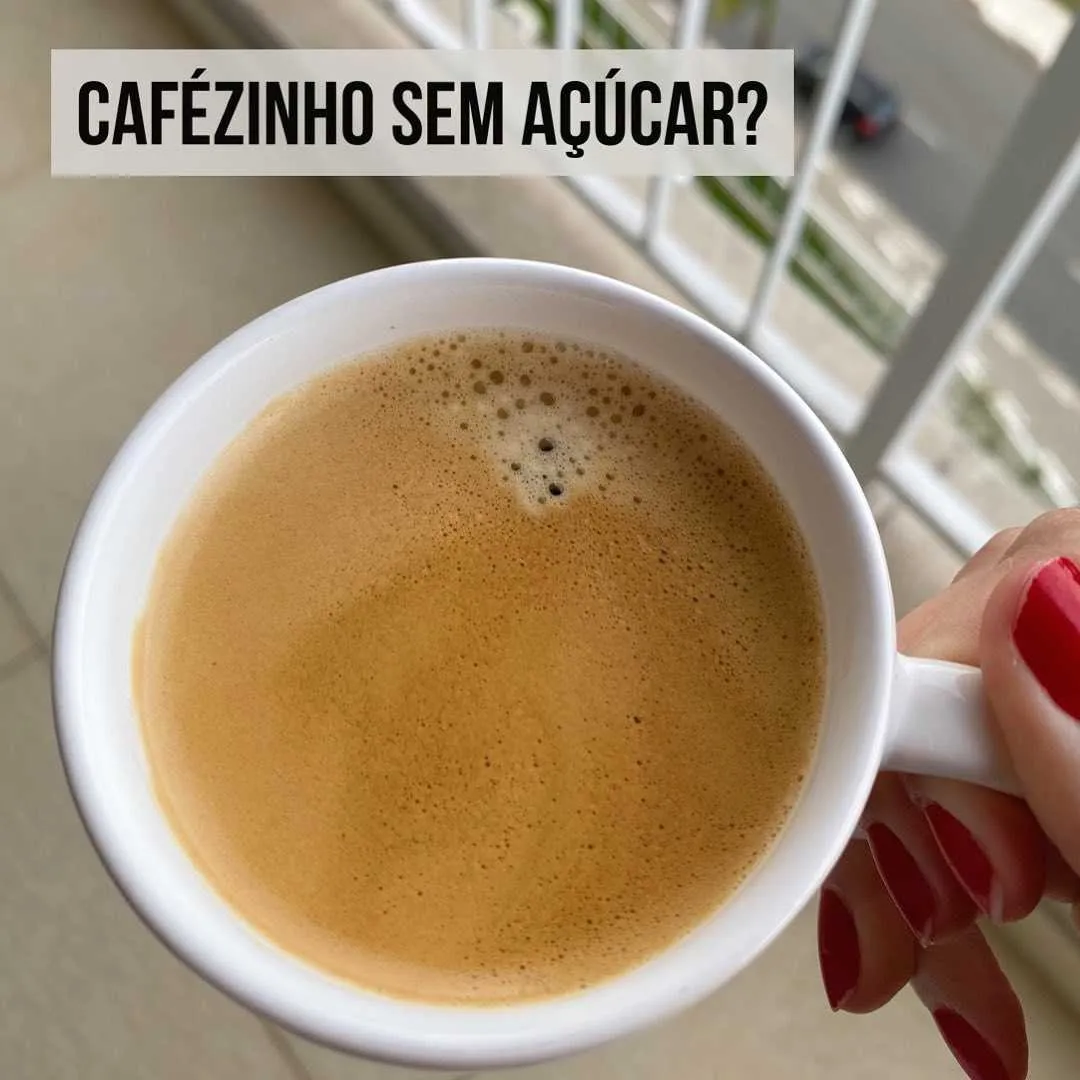 Mão segurando xícara branca de cafézinho sem açúcar visto de cima, com crema na superfície