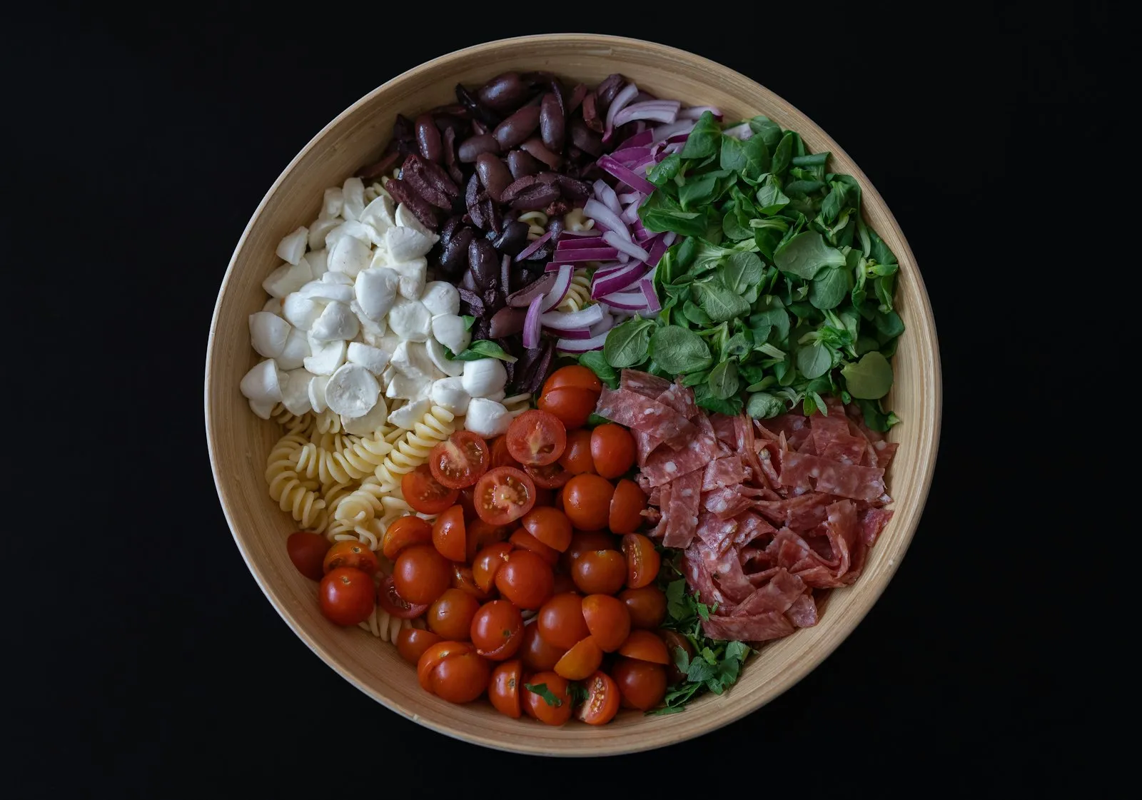 Salada de macarrão rica em carboidrato com tomate, mussarela, azeitona, salame e folhas em tigela
