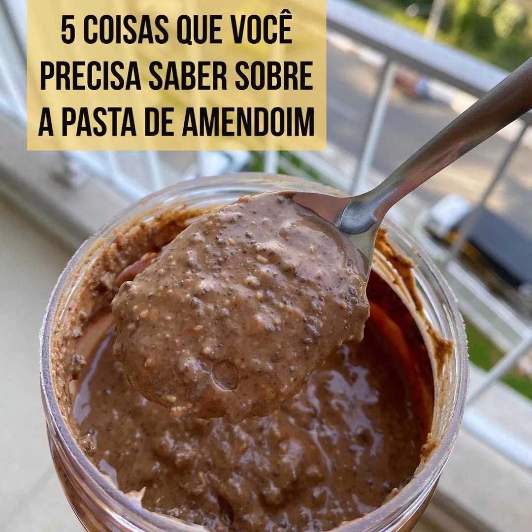 Colher cheia de pasta de amendoim integral sendo retirada de pote aberto