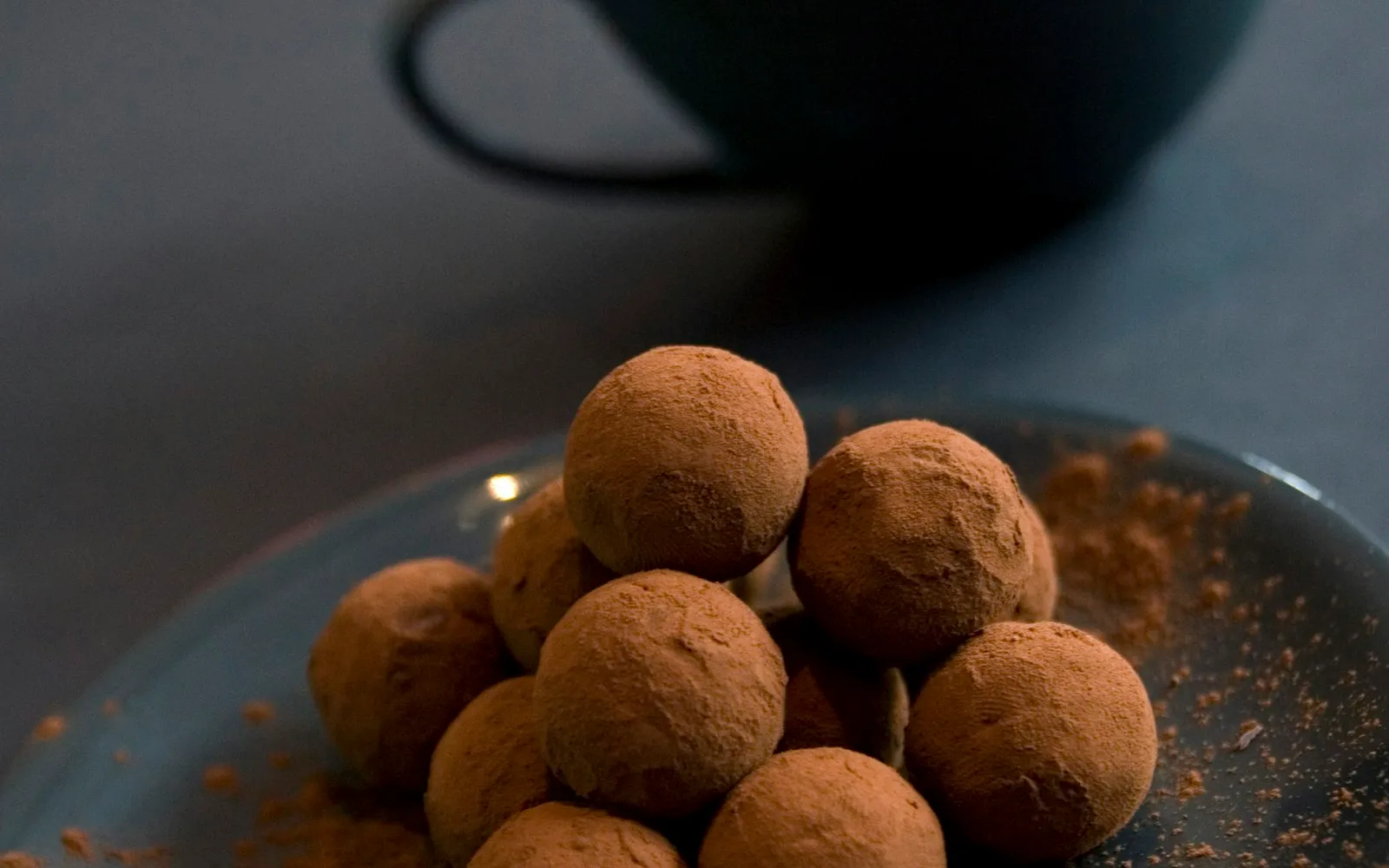 Brigadeiros de chocolate polvilhados com cacau empilhados em prato, sobre a vontade de doce todo dia
