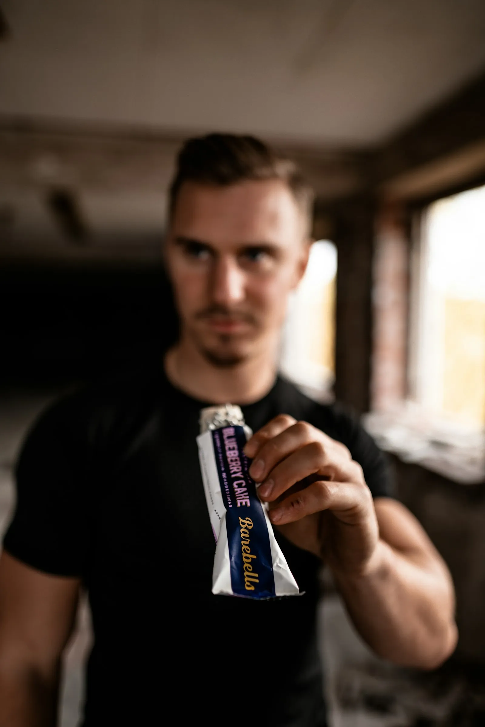 Homem de camiseta preta segurando uma barra de proteína embalada, tema de suplementação e gel de carboidrato